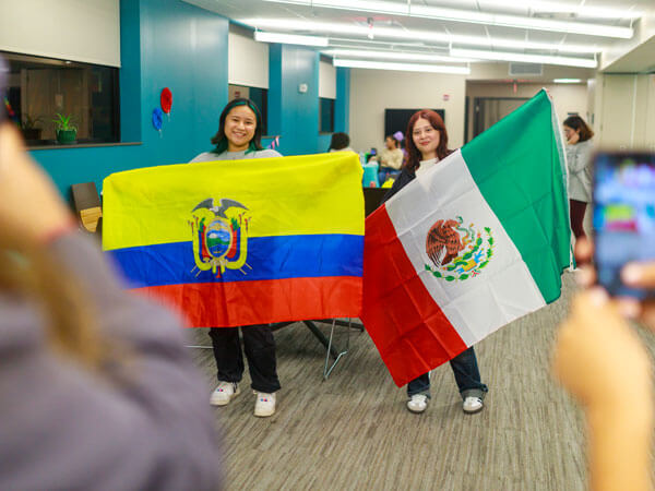 Two students holding flags pose for a photo.